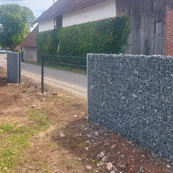 Díl sypané gabionové stěny se šedým kamenem vedle plotu z 2D panelů